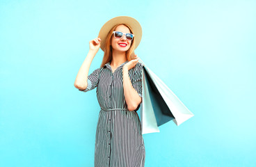 Wall Mural - Fashion smiling woman with shopping bags in striped dress, round straw hat on blue background