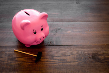 Piggy bank. Moneybox in shape of pig near hammer on dark wooden background copy space