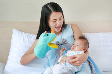 Wall Mural - Asian mother playing animal puppet with her baby on the bed room at home.
