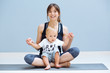 © Iryna - Happy sportive brunette mother hugging and playing with her lovely bay toddler son while sitting on floor over grey background. Fitness, happy maternity yoga with children concept.