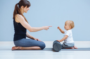 Wall Mural - Young mother workout with foam rollers does physical pilates exercises together with her toddler baby boy. Fitness, happy maternity sport with children concept.