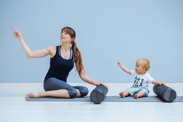 Wall Mural - Young mother workout with foam rollers does physical pilates exercises together with her toddler baby boy. Fitness, happy maternity sport with children concept.