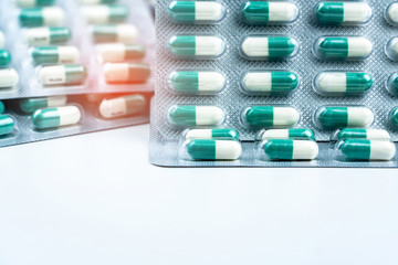 Canvas Print - Green-white small capsule pills in blister packs on white table and blurred background of pills pack. Vitamins and supplements. Health care concept. Pharmaceutical industry and pharmacy background.