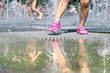 A girl with wet legs in pink slippers play in the summer in the fountain of the city park