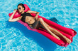© LIGHTFIELD STUDIOS - asian girl in black swimsuit relaxing on pink inflatable mattress in swimming pool