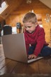 © Wavebreak Media - Boy using laptop while sitting on wooden floor at home