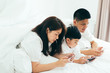 © ic36006 - Asian boy playing smartphone with young parents lying in bed.Happy famility