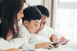 © ic36006 - Asian boy playing smartphone with young parents lying in bed.Happy famility
