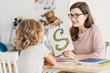 © Photographee.eu - A child with development problems with a professional speech therapist during a meeting. Tutor holding a prop poster of a snake as a letter 's'.