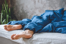Cropped Image Of Sleeping Mens Legs Under Blanket In Bed At Home