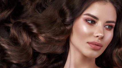 Wall Mural - Beautiful brunette model with curls, classic makeup and full lips. The beauty of the face. Portrait shot in the studio.