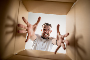 The surprised man unpacking, opening carton box and looking inside. The package, delivery, surprise, gift lifestyle concept. Human emotions and facial expressions concepts