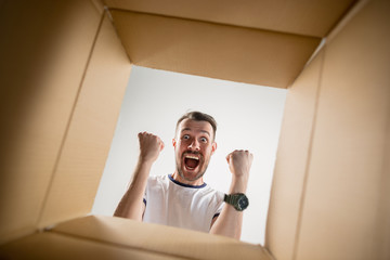 The surprised man unpacking, opening carton box and looking inside. The package, delivery, surprise, gift lifestyle concept. Human emotions and facial expressions concepts