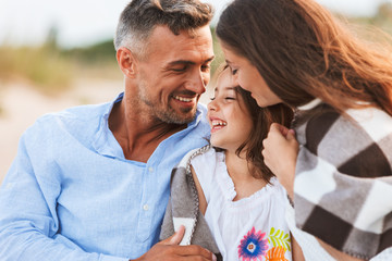 Parents hugging outdoors at the beach with their daughter.