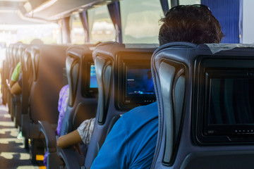 The man on the passenger seat of the bus listens to music and looks at the tablet. He looks at the device's screen and smiles. Outside the window is a beautiful green landscape.