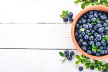 Blueberries With Leaves In A Wooden Plate. On A Wooden Background. Top View. Free Space For Your Text.