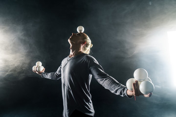 Wall Mural - Blond juggler with white balls on black background