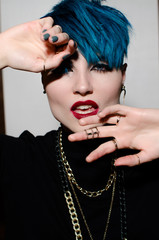 Fashion shot of a woman whith bright blue hair covered her face with her hands on isolated gray wall background. Professional model posing for magazine cover