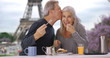 Older white male and female near Eiffel Tower eat delicious breakfast pastry