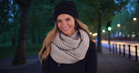 Wall Mural - Smiling woman in cozy hat and scarf outside at night