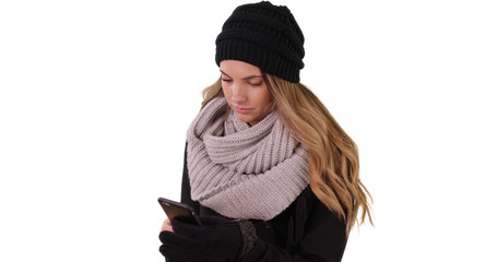 Wall Mural - Woman in cozy hat and scarf texting with mobile device on white background
