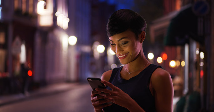 Wall Mural -  - Pretty smiling African American female reads text message on the street at night
