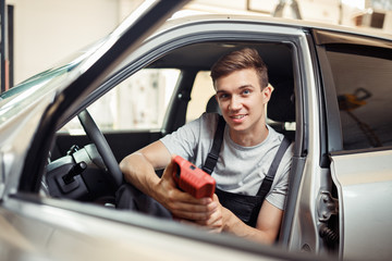 Wall Mural - A young mechanic is at work sitting in a car while checking it