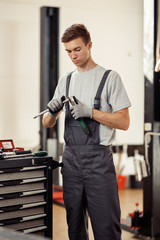 Wall Mural - An attractive young man holding special instruments in his hands is at work in a car service