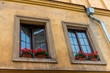 pots with red geranium on the windowsills of the yellow house in the city close up
