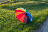 Fototapeta Tęcza - Beautiful girl plays on nature with a colorful umbrella. Rainbow umbrella in the hands of the child