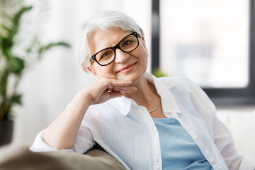 Canvas Print - vision, age and people concept - portrait of happy senior woman in glasses sittin on sofa at home