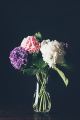 pink, white and purple hortensia flowers in glass vase, on black