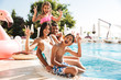 © Drobot Dean - Image of attractive caucasian family with children sitting near luxury swimming pool, with pink rubber ring outside hotel