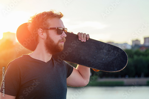 Photographie happy californian beautiful bearded red-haired sexy man in sunflasses holds a skateboard (longboard) at sunset on the beach
