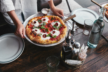 cropped shot of woman carrying plate with pizza margherita to serve on table at restaurant