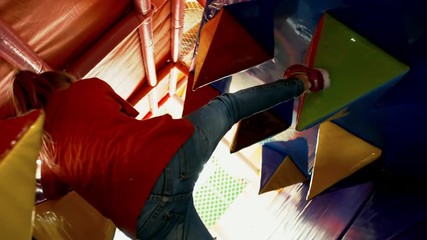 Wall Mural - Rear view of active little girl of primary school age climbing inflatable spikes in play tunnel when having fun in indoor amusement park