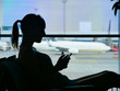 SILHOUETTE: Female tourist waiting for her flight and looking at her smartphone.