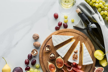 Wall Mural - flat lay with wine, cheese, jamon and various fruits arranged on wooden board on white marble tabletop