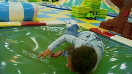 Wall Mural - Happy black girl of elementary school age jumping and lying on water bed in indoor amusement park