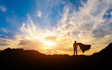 Silhouette of a successful man with a raincoat on a mountain on a sunset background.