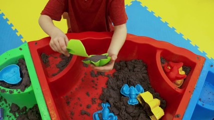 Wall Mural - Medium shot of playful little girl of elementary school age forming various shapes using sand molds and shovel when spending time in playroom