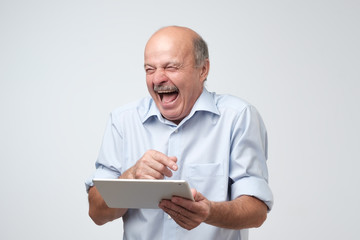 Poster - Cheerful mature european man laughing holding tablet