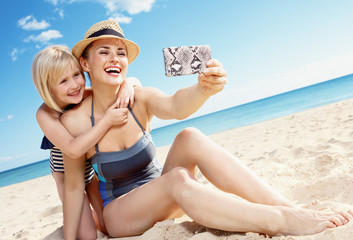 Wall Mural - mother and daughter taking selfie with smartphone on seacoast