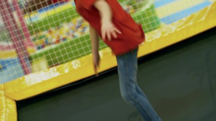 Wall Mural - Dutch angle view of young girl of primary school age having fun jumping on indoor trampoline in playroom