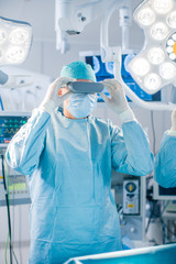 Wall Mural - Surgeons Put on Augmented Reality Glasses to Perform State of the Art Surgery in High Tech Hospital. Doctors and Assistants Working in Operating Room.