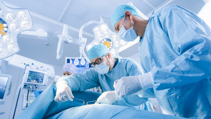 Wall Mural - Low Angle Shot of a Diverse Team of Professional Surgeons Performing Invasive Surgery on a Patient in the Hospital Operating Room. Surgeons Use Instruments