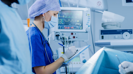 Wall Mural - In the Hospital Operating Room Anesthesiologist Looks and Monitors and Controls Patient's Vital Signs, Nodding to a Chief Surgeon to Proceed with Surgery.