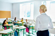 © LIGHTFIELD STUDIOS - rear view of teacher looking at children sitting at classroom