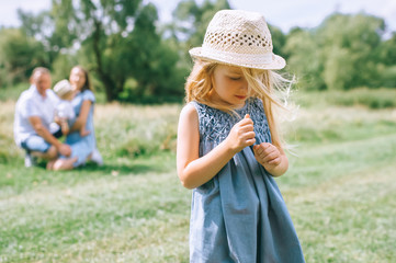 Wall Mural - adorable blonde girl in straw hat with family behind