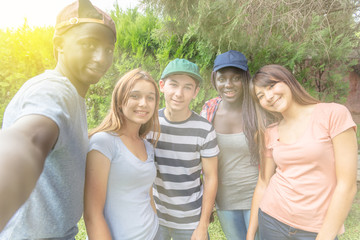 Multi ethnic group of teenagers happy outdoor making selfies. Sun rays coming from the sky